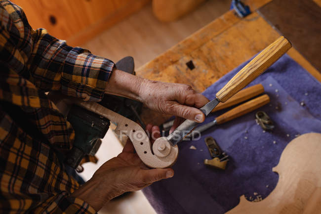 Primer plano de la luthier femenina trabajando en el pergamino de un violín en su taller - foto de stock