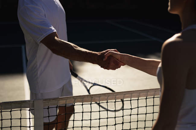 Vue de côté gros plan d'une jeune femme caucasienne et d'un homme serrant la main après un match de tennis terminé — Photo de stock