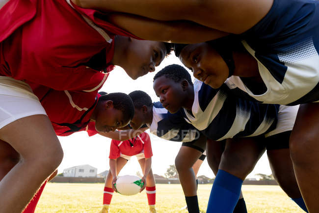 Vista lateral de cerca de dos equipos opuestos de jóvenes jugadoras de rugby multiétnicas adultas en un scrum, esperando a que la pelota sea lanzada durante un partido de rugby - foto de stock