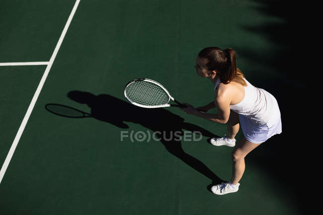 Vista laterale di una giovane donna caucasica che gioca a tennis in una giornata di sole, tiene in mano una racchetta e aspetta la palla — Foto stock