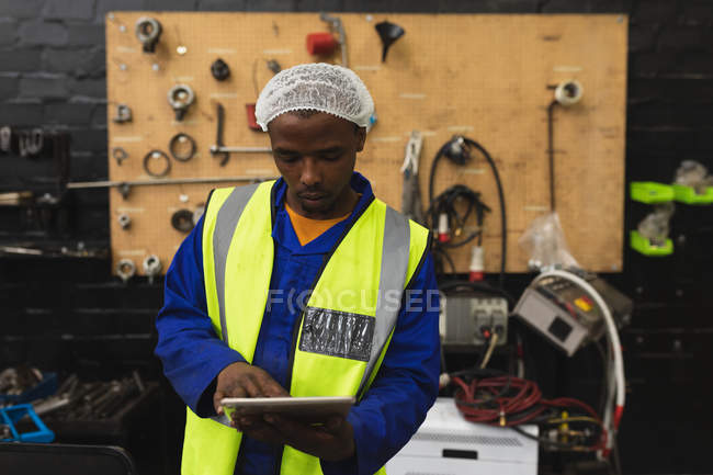 Nahaufnahme eines jungen afrikanisch-amerikanischen Fabrikarbeiters mit einem Tablet-Computer in der Maschinenhalle eines Verarbeitungsbetriebs, im Hintergrund Geräte und Werkzeuge — Stockfoto