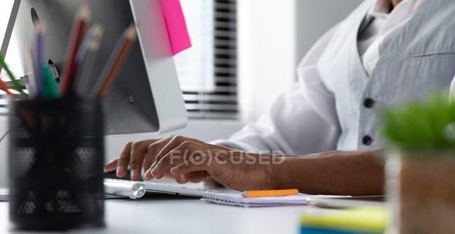 Vista lateral sección media del hombre sentado en un escritorio usando una computadora en la oficina moderna de un negocio creativo - foto de stock