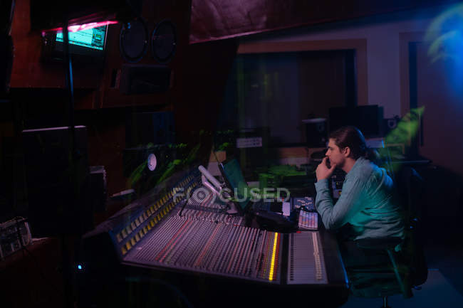 Vista lateral de un joven ingeniero de sonido caucásico sentado y trabajando en un escritorio de mezclas en un estudio de grabación - foto de stock