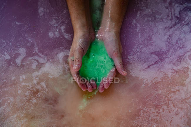 Primo piano delle mani coppettate di una donna in un bagno contenente sali da bagno verdi effervescenti nell'acqua del bagno rosa — Foto stock