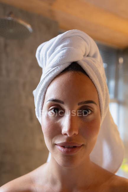 Porträt einer jungen kaukasischen Brünetten mit in ein Handtuch gehüllten Haaren, die in einem modernen Badezimmer in die Kamera lächelt — Stockfoto
