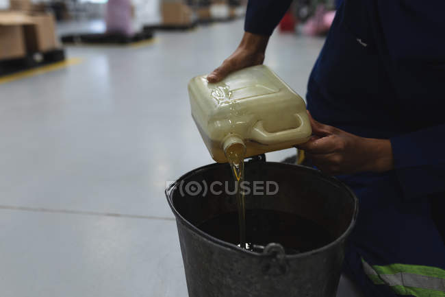Вид збоку посередині чоловіка працівник заводу заливає рідину з пластикового контейнера до відра на складі на переробному заводі — стокове фото