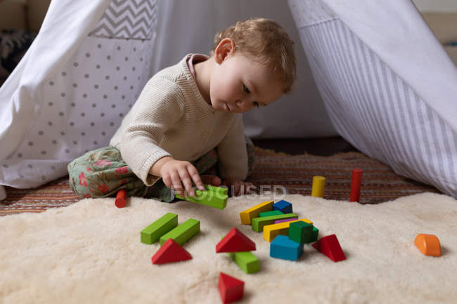 Vista frontal de cerca de un bebé caucásico sentado en el suelo y jugando con bloques de madera, descalzo - foto de stock