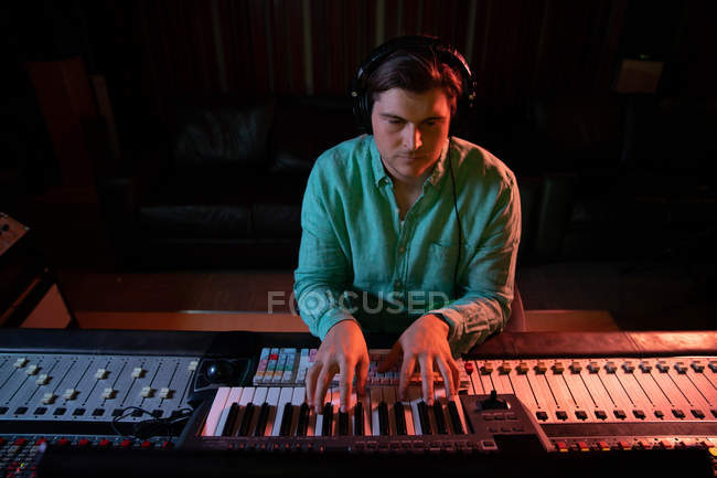 Nahaufnahme eines jungen kaukasischen männlichen Tontechnikers, der an einem Mischpult in einem Tonstudio sitzt und eine Midi-Tastatur benutzt — Stockfoto