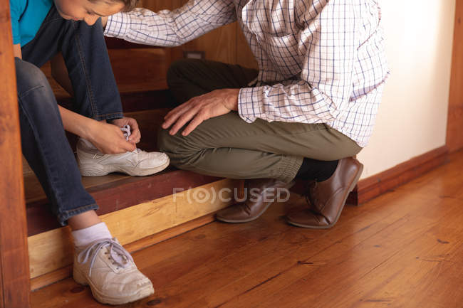 Vista lateral de cerca de un hombre caucásico de mediana edad sentado en una escalera con su hijo preadolescente, el niño está atando cordones - foto de stock