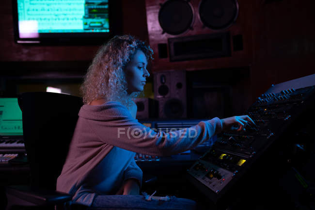 Side view close up of a young Caucasian female sound engineer sitting and working at a mixing desk in a recording studio — Stock Photo
