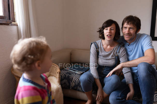Front view close up of a young Caucasian father and mother sitting on a sofa and smiling and looking at their baby — Stock Photo