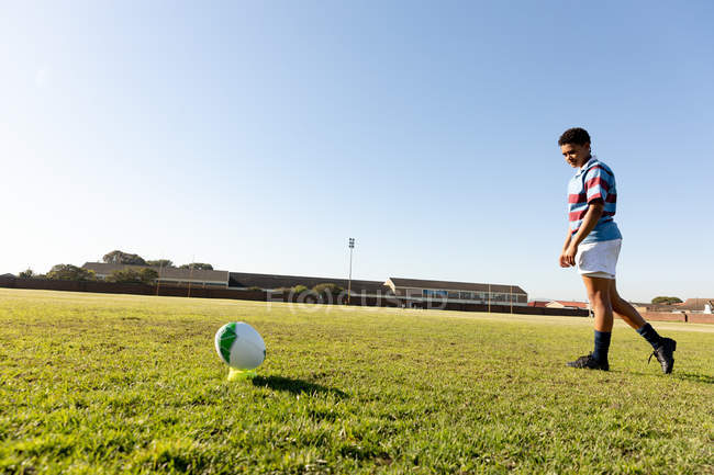 Side view of a young adult mixed race female rugby player standing on a rugby pitch preparing to run up to the ball and make a place kick — Stock Photo