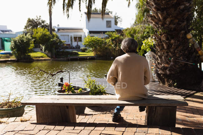 Заднього виду старших кавказька жінка сидить на лавці біля озера — стокове фото