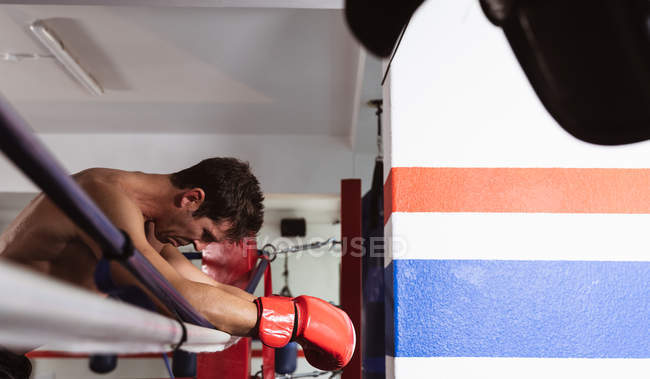 Vista lateral de cerca de un joven boxeador caucásico apoyado en una cuerda de un anillo de boxeo - foto de stock
