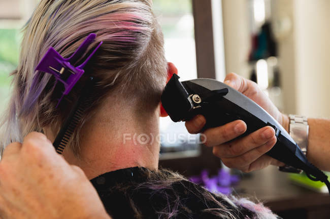 Vue arrière gros plan d'un coiffeur caucasien d'âge moyen et d'une jeune femme caucasienne se faisant couper les cheveux dans un salon de coiffure — Photo de stock