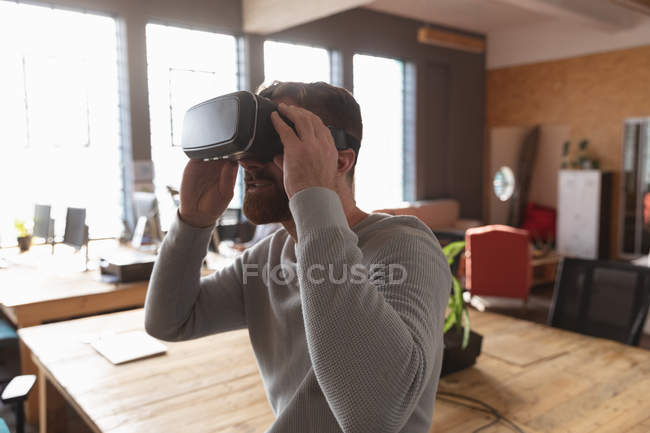 Vista lateral de cerca de un joven caucásico con un casco VR en una oficina creativa - foto de stock