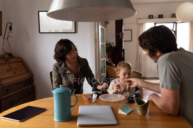Vista frontale di una giovane madre e padre caucasici seduti a un tavolo e che nutrono il loro bambino — Foto stock