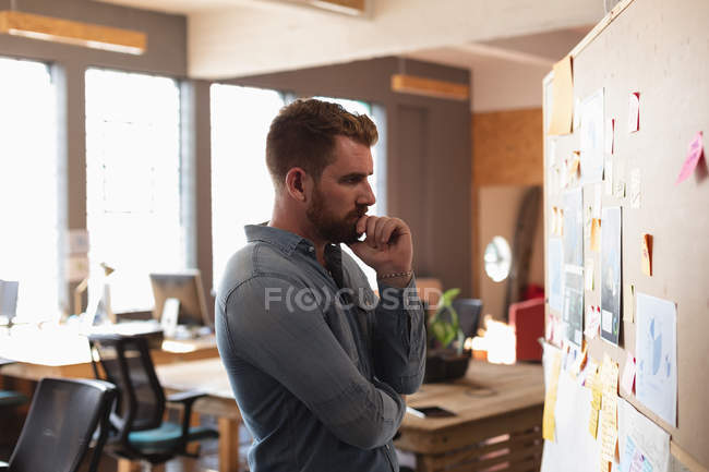 Seitenansicht eines jungen kaukasischen Mannes, der Notizen an einer Wand liest und während eines Team-Brainstormings in einem Kreativbüro denkt — Stockfoto