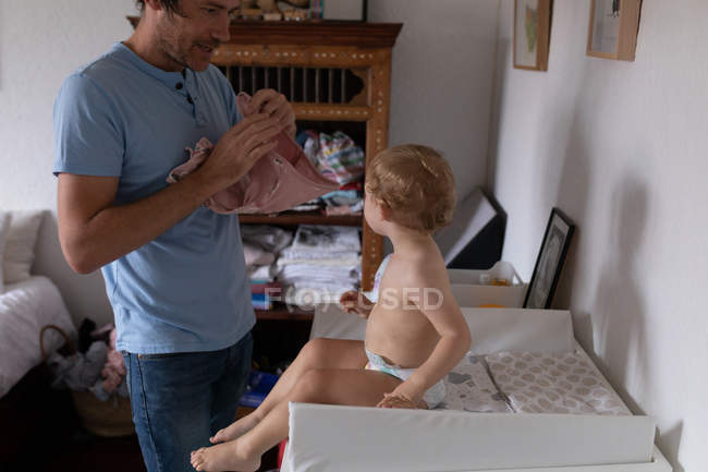 Vista laterale di un giovane padre caucasico che fa vestire il suo bambino su un fasciatoio — Foto stock