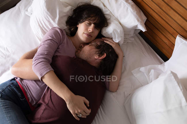 Vue de face gros plan d'un jeune homme et d'une jeune femme caucasiens dormant et embrassant dans un lit — Photo de stock