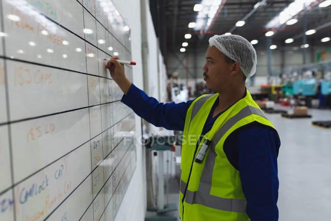 Side view close up of a middle aged mixed race male factory worker updating information on a whiteboard in a warehouse at a processing plant — Stock Photo