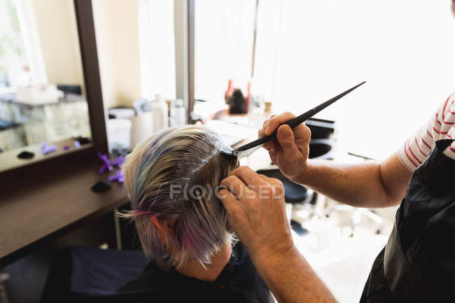 Visão traseira close-up de um cabeleireiro masculino caucasiano de meia idade e uma jovem mulher caucasiana ter seu cabelo colorido em um salão de cabeleireiro — Fotografia de Stock
