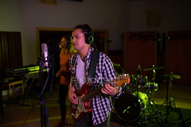 Vue latérale d'une jeune chanteuse caucasienne et d'un jeune guitariste chanteur mixte se produisant lors d'une session dans un studio d'enregistrement — Photo de stock