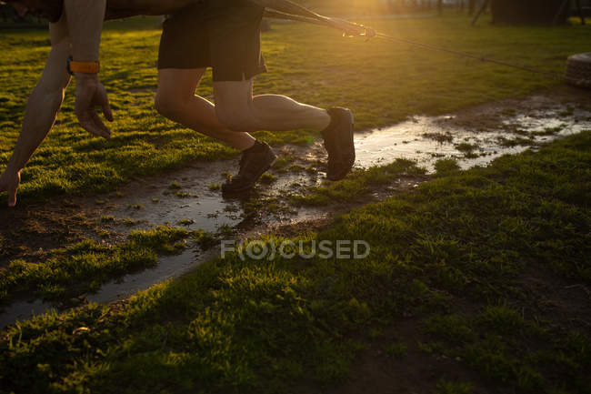 Side view low section of man pulling a tyre on a rope around his waist through mud at an outdoor gym during a bootcamp training session — Stock Photo