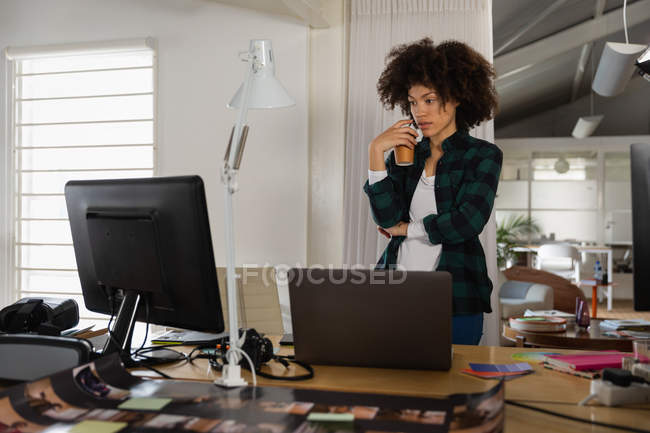 Передній вигляд молодої змішаної жінки, що стоїть і дивиться на екран комп'ютера в творчому офісі — стокове фото