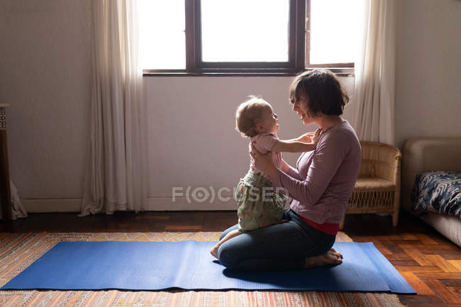 Vue latérale d'une jeune mère caucasienne assise sur un sol et tenant son bébé, se regardant — Photo de stock