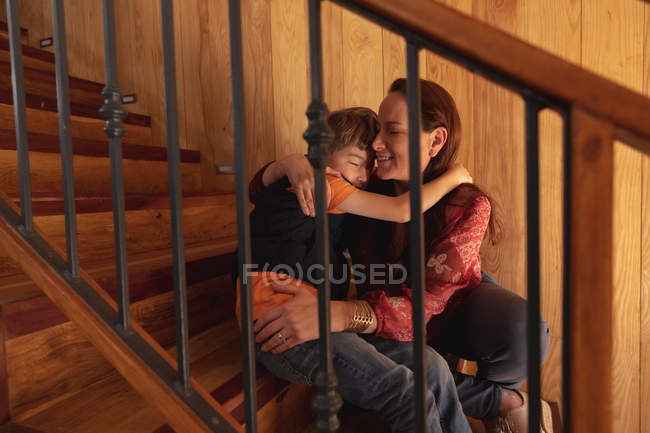 Vista frontal close-up de uma mulher caucasiana de meia idade abraçando com seu filho pré-adolescente sentado em uma escada — Fotografia de Stock