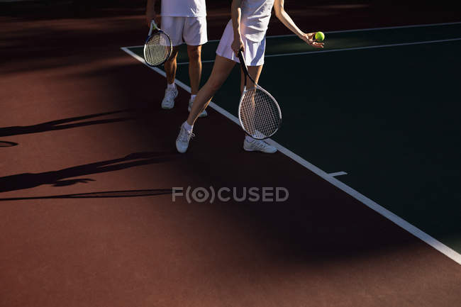 Vista lateral da mulher e um homem jogando tênis em um dia ensolarado, mulher se preparando para servir — Fotografia de Stock