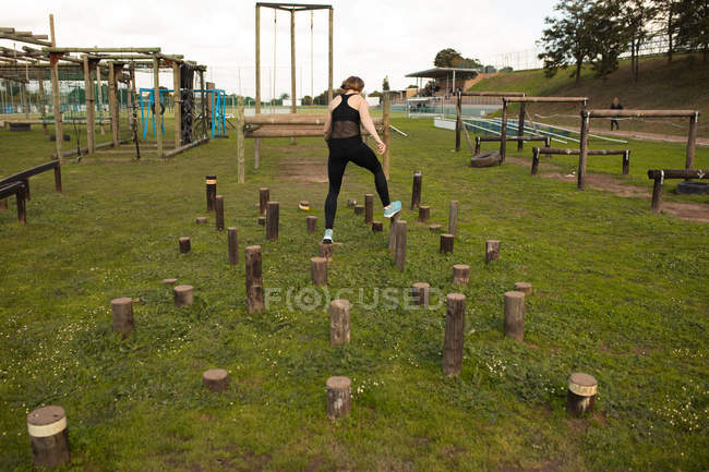 Vue arrière d'une jeune femme caucasienne sautant entre des poteaux en bois dans une salle de gym extérieure lors d'une séance d'entraînement de bootcamp — Photo de stock