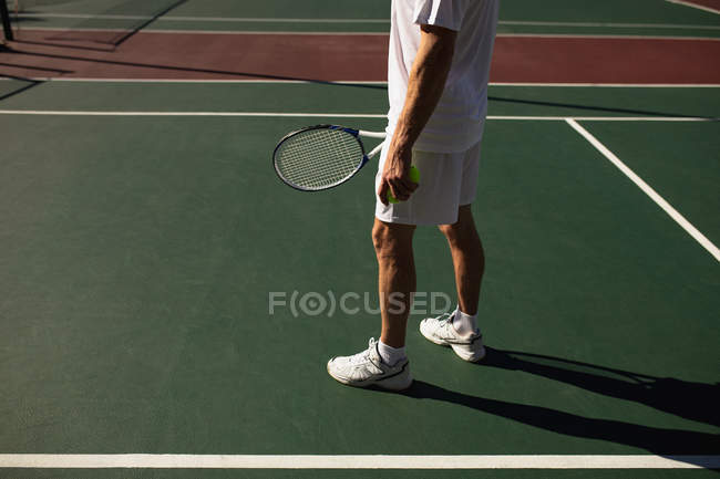Vista lateral do homem jogando tênis em um dia ensolarado, segurando uma raquete e bolas — Fotografia de Stock