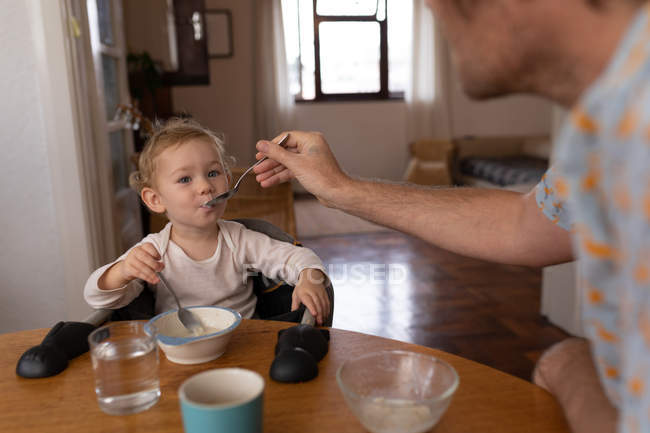 Передній вигляд молодого кавказького батька, який годує своє дитя ложечкою. — стокове фото