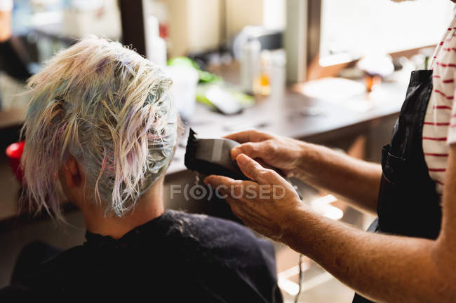 Вид сзади на белого парикмахера средних лет и молодую белую женщину с подстриженными волосами в парикмахерской — стоковое фото