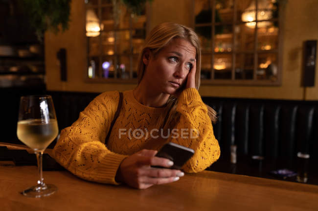 Вид на молоду Кавказьку жінку розслабляє на відпочинку в барі, випиваючи вино і за допомогою смартфона — стокове фото