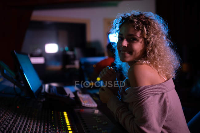 Vista laterale da vicino di una giovane ingegnere del suono caucasica seduta e che lavora ad un mixer in uno studio di registrazione, si gira verso una telecamera sorridente — Foto stock