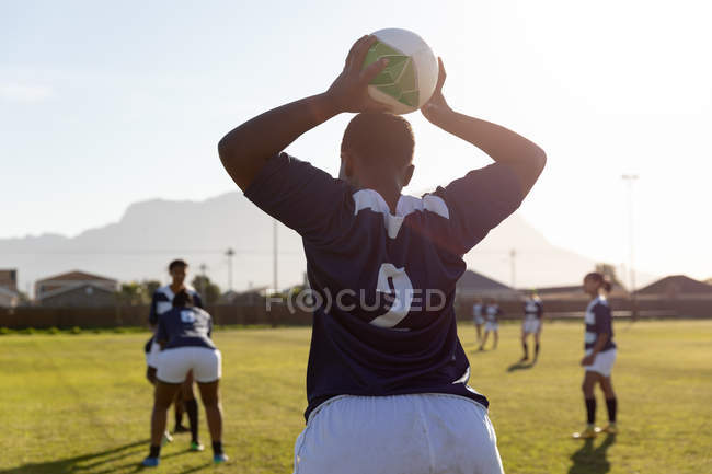 Rear view of a young adult mixed race female rugby player preparing to throw the ball to teammates during a rugby match — Stock Photo