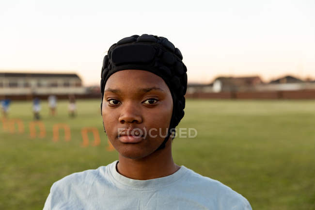 Retrato de uma jovem adulta de raça mista jogadora de rugby usando um protetor de cabeça em um campo esportivo olhando para a câmera — Fotografia de Stock