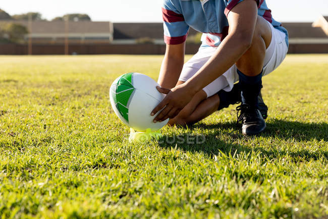 Нижняя секция женского регбиста, стоящая на коленях на поле для регби и бросающая мяч на мячик для удара по месту — стоковое фото