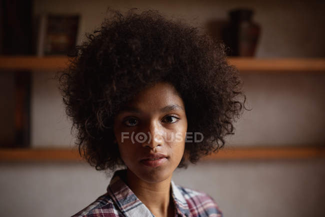 Retrato close-up de uma jovem mulher de raça mista vestindo uma camisa marcada olhando direto para a câmera em casa — Fotografia de Stock