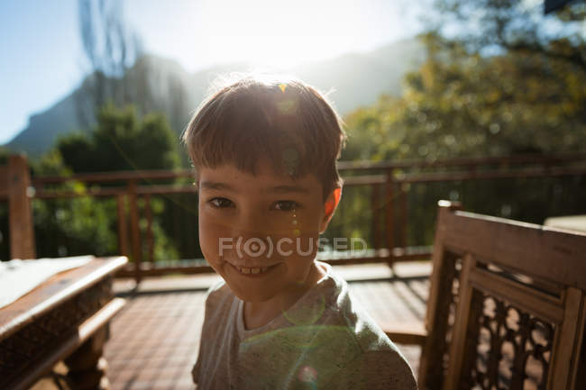 Retrato de cerca de un niño caucásico preadolescente sentado en una mesa en un jardín, sonriendo a la cámara - foto de stock