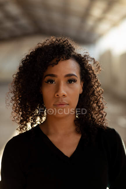 Portrait close up of a young mixed race female ballet dancer with shoulder length curly hair looking straight to camera in an empty warehouse — Stock Photo
