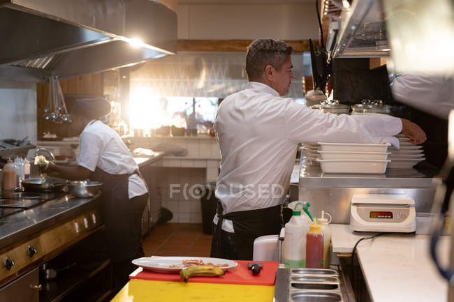 Side view close up of a middle aged Caucasian male chef and a young African American female chef busy working in a restaurant kitchen — Stock Photo