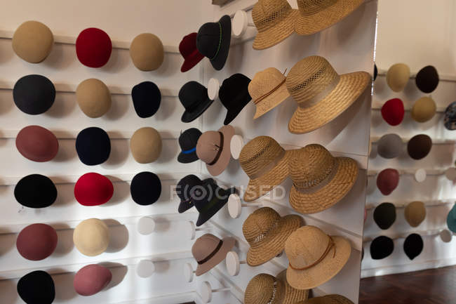Various styles of hats displayed in rows on the white walls of the showroom at a hat makers — Stock Photo