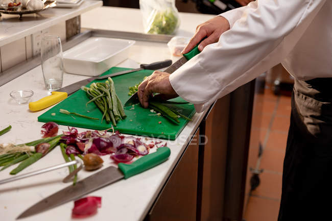 Vista lateral sección media de chef masculino picando verduras en un mostrador en una cocina de restaurante - foto de stock