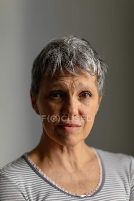 Retrato de cerca de una mujer caucásica madura con el pelo gris corto mirando directamente a la cámara con una expresión incierta - foto de stock