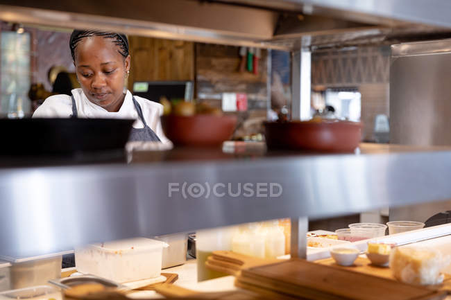 Вид спереди на молодую афроамериканку-повара, работающую на кухне ресторана. — стоковое фото