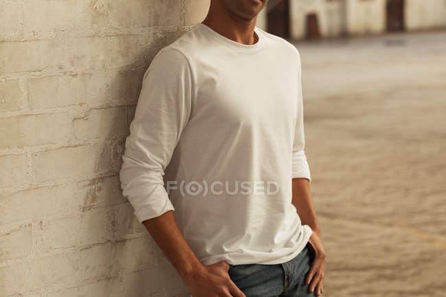 Side view mid section of a young man leaning against a pillar with his thumbs in the pockets of his jeans in an empty room at an abandoned warehouse — Stock Photo